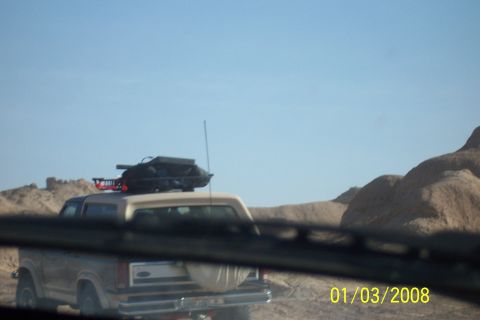 1990 Ford Bronco - Tan 1990 Ford Bronco driving in a desert environment, equipped with a roof rack and cargo box.