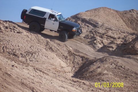 1990 Ford Bronco - A two-tone Ford Bronco navigates a steep, sandy incline under a clear blue sky.