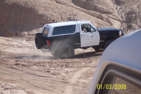 1990 Ford Bronco - This two-tone Ford Bronco navigates a dusty off-road trail, its rear tire kicking up a cloud of dirt.