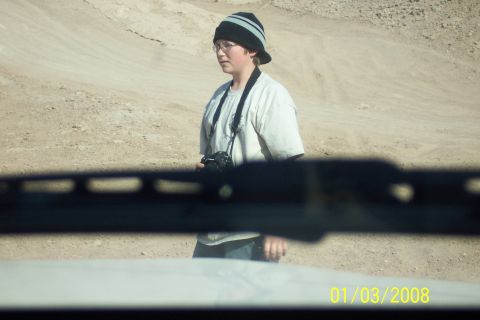 1990 Ford Bronco - A person stands in a dusty, desert environment, holding a camera around their neck.