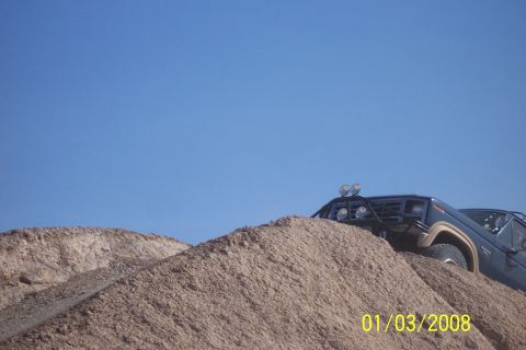1990 Ford Bronco - A dark blue SUV navigates a steep dirt incline under a clear blue sky.