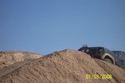 1990 Ford Bronco - A dark blue 1990 Ford Bronco navigates a steep sandy incline under a clear blue sky.