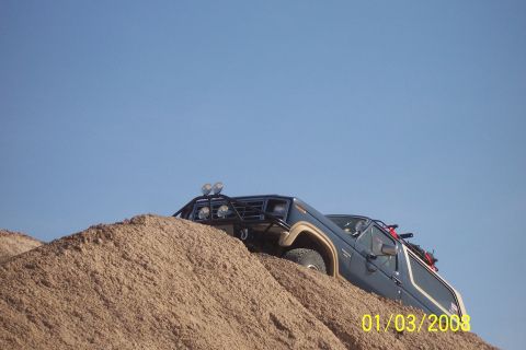 1990 Ford Bronco - Ford Bronco navigates a steep sand dune under a clear blue sky.