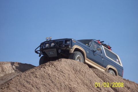 1990 Ford Bronco - A Ford Bronco navigates a steep dirt incline under a clear blue sky.