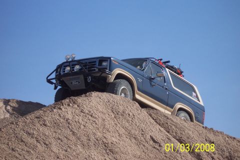 1990 Ford Bronco - This blue 1990 Ford Bronco is equipped for off-road adventures, climbing a sandy incline under a clear blue sky.