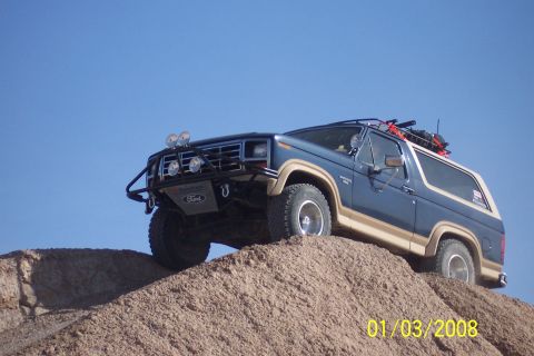 1990 Ford Bronco - Off-road Bronco ascends a sandy incline under a bright blue sky.