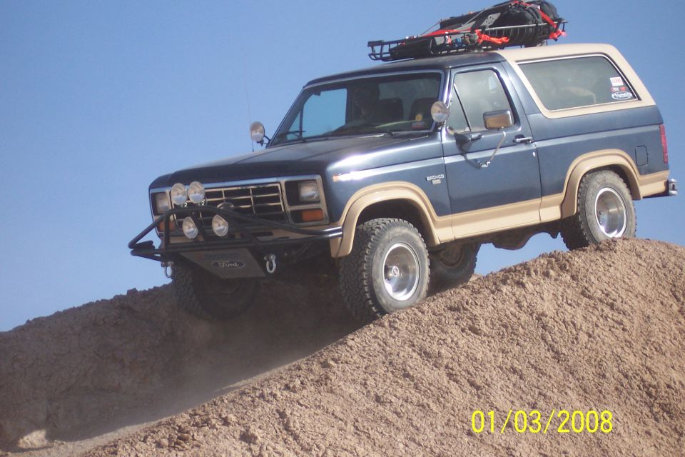 Blue and tan Ford Bronco with roof rack driving up a dirt hill
