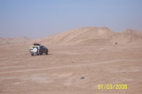 1990 Ford Bronco - A lone SUV navigates a vast, arid desert landscape under a clear blue sky.
