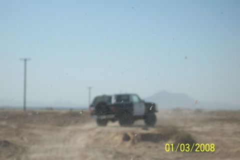 1990 Ford Bronco - A 1990 Ford Bronco is seen from a 3/4 front angle driving on a dirt road in a desert landscape.