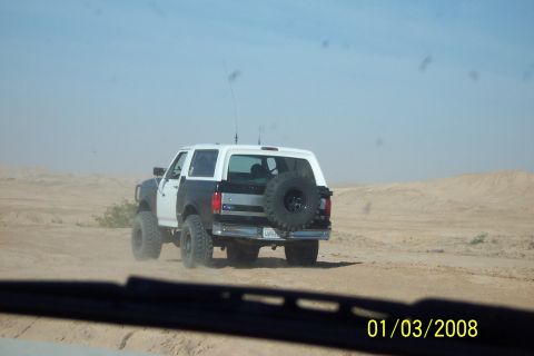 1990 Ford Bronco - This 1990 Ford Bronco, seen from behind, kicks up dust as it travels on a desert road with a spare tire mounted on its rear.