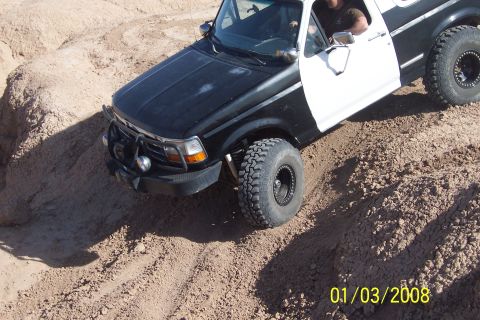 1990 Ford Bronco - This Ford Bronco, likely from the early 1990s, navigates a sandy terrain with its distinctive two-tone paint and modified wheels.