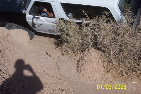1990 Ford Bronco - A Ford Bronco navigates a challenging dirt path, with thorny bushes encroaching on the trail.