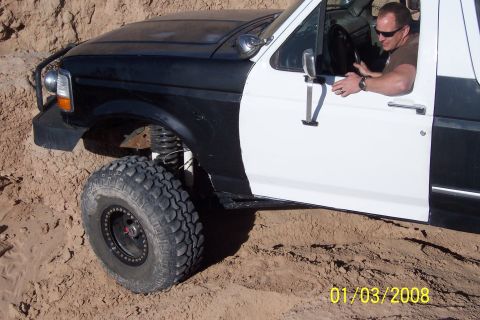 1990 Ford Bronco - A driver operates a modified Ford Bronco off-road, its two-tone paint and lifted suspension evident.