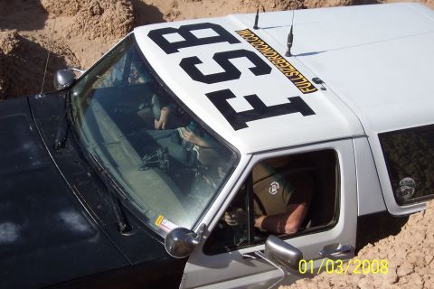 1990 Ford Bronco - A Ford Bronco is stuck in the dirt with large lettering on its roof.