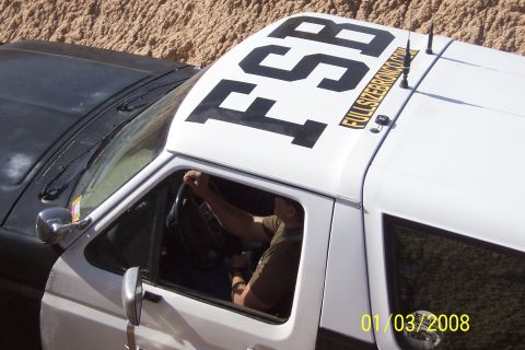 1990 Ford Bronco - A white Ford Bronco with black lettering on the roof is seen from a high angle, with a driver inside.