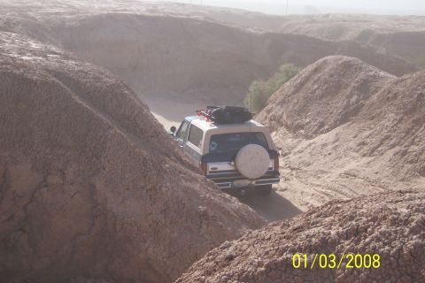 1990 Ford Bronco - A Ford Bronco navigates a dusty, off-road trail through a barren, hilly landscape.
