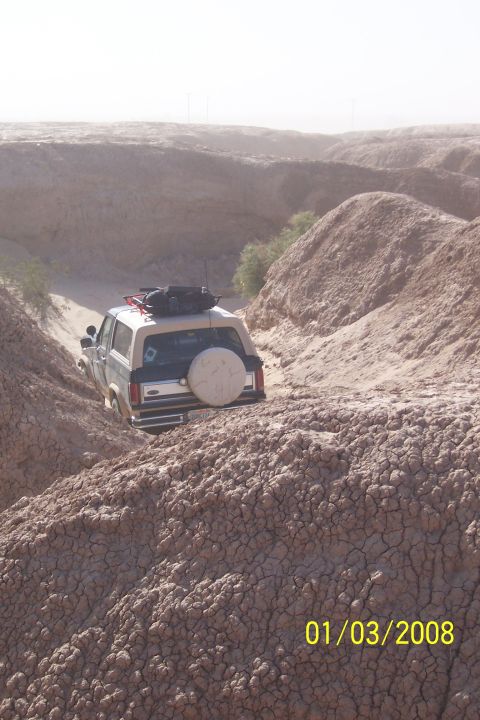 1990 Ford Bronco - A 1987 Ford Bronco navigates a narrow, dry canyon with cracked earth and sparse vegetation.