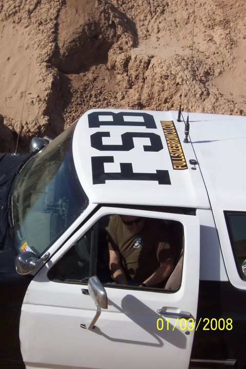 1990 Ford Bronco - A white and black Ford Bronco is parked in a sandy, rocky area. The vehicle has large black lettering on its roof.