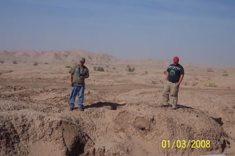 1990 Ford Bronco - Two men stand in a barren, dusty desert landscape under a clear blue sky.