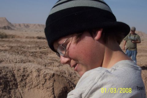 1990 Ford Bronco - A person in a beanie and glasses looks down in a desert environment with another person in the distance.