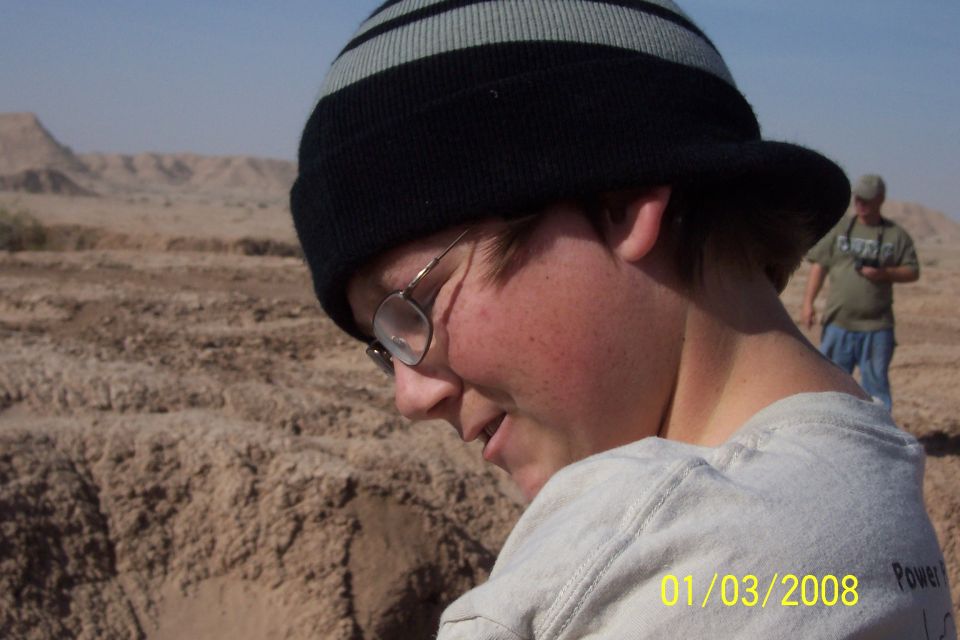 Person wearing a beanie and glasses in a desert with another person in the background