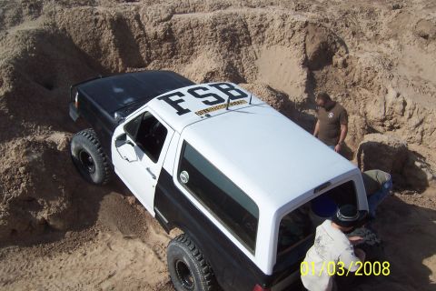 1990 Ford Bronco - A modified Ford Bronco navigates a sandy terrain with assistance from onlookers.