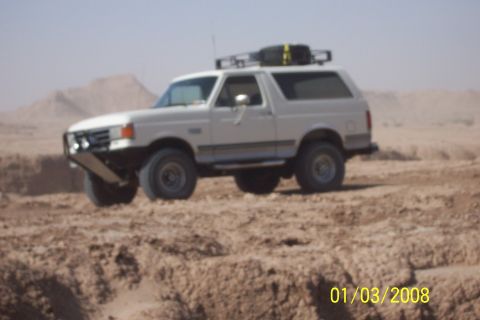1990 Ford Bronco - A white 1990 Ford Bronco navigates a desert landscape with a roof rack and custom bumper.