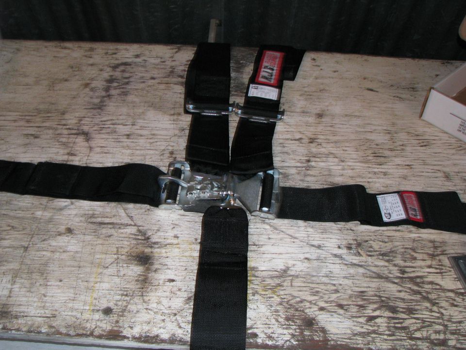 Black RJS racing harness with central buckle on a wooden table.