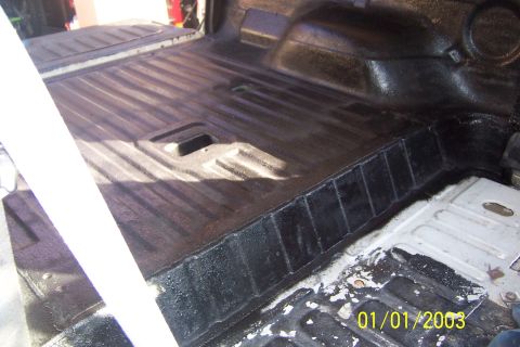 1990 Ford Bronco - The bed of a vehicle, possibly a pickup truck or SUV, is shown with a dark protective coating applied to the floor and sides. The ribbed me…