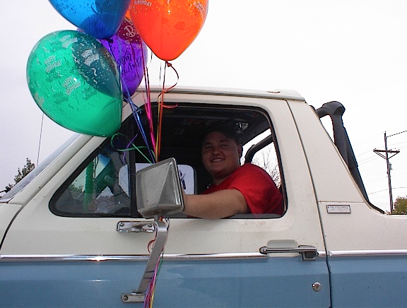White and light blue 1978 Ford Bronco side view with a man inside holding balloons