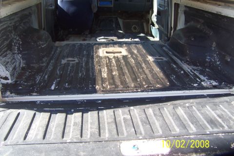 1990 Ford Bronco - The interior of a pickup truck bed is shown from the tailgate looking forward. The bed floor has a ribbed texture with some white residue a…