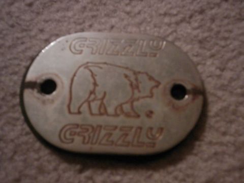 1987 Ford Bronco - A silver oval metal plate with a bear silhouette and the word "GRIZZLY" embossed twice is shown against a textured brown background. Two ho…