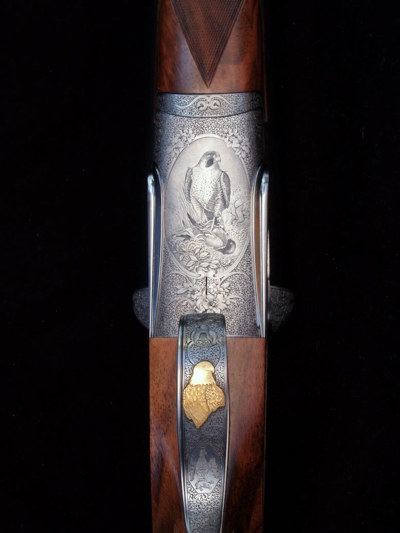 Close-up of ornate shotgun receiver with bird engravings and gold eagle inlay.