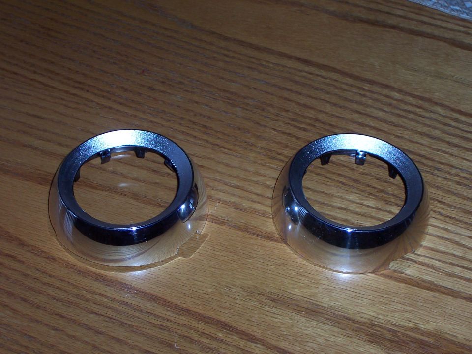 Two chrome trim rings with black plastic tabs on a wooden surface