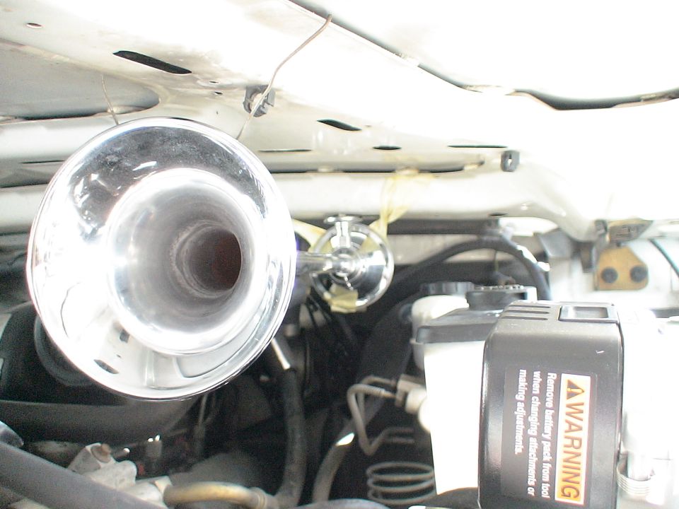 Chrome air horn mounted under vehicle hood with warning sticker.