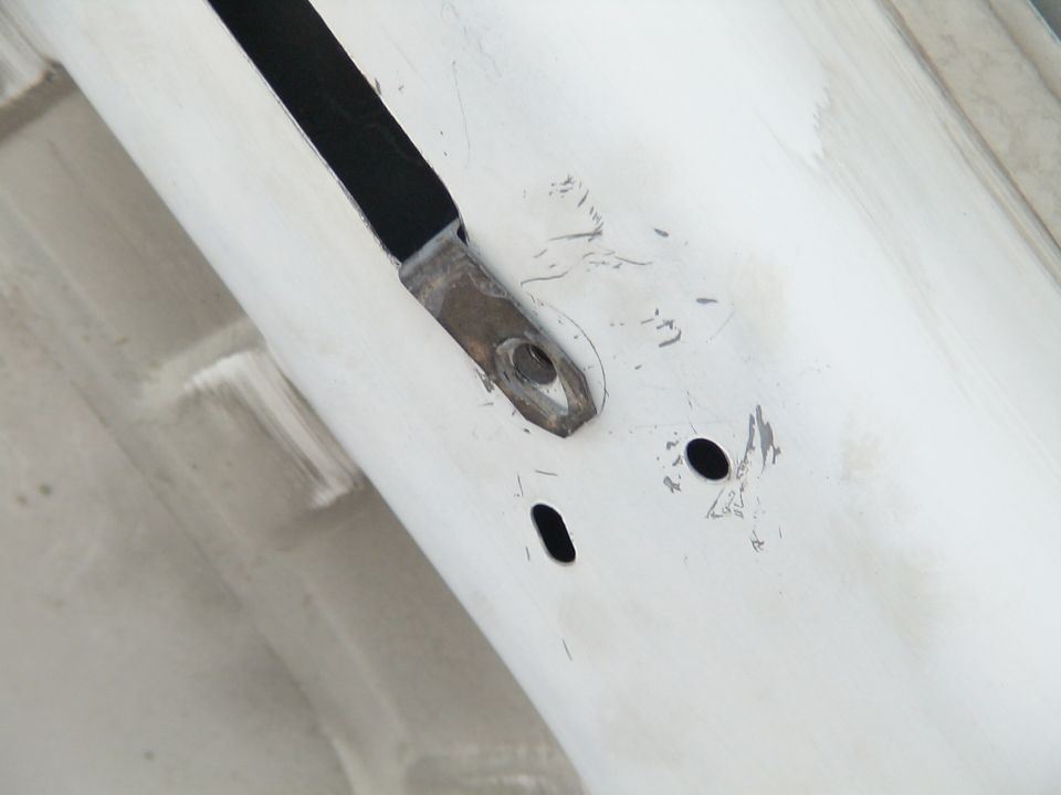 Close-up of white vehicle body panel with metal bracket and two oval holes.