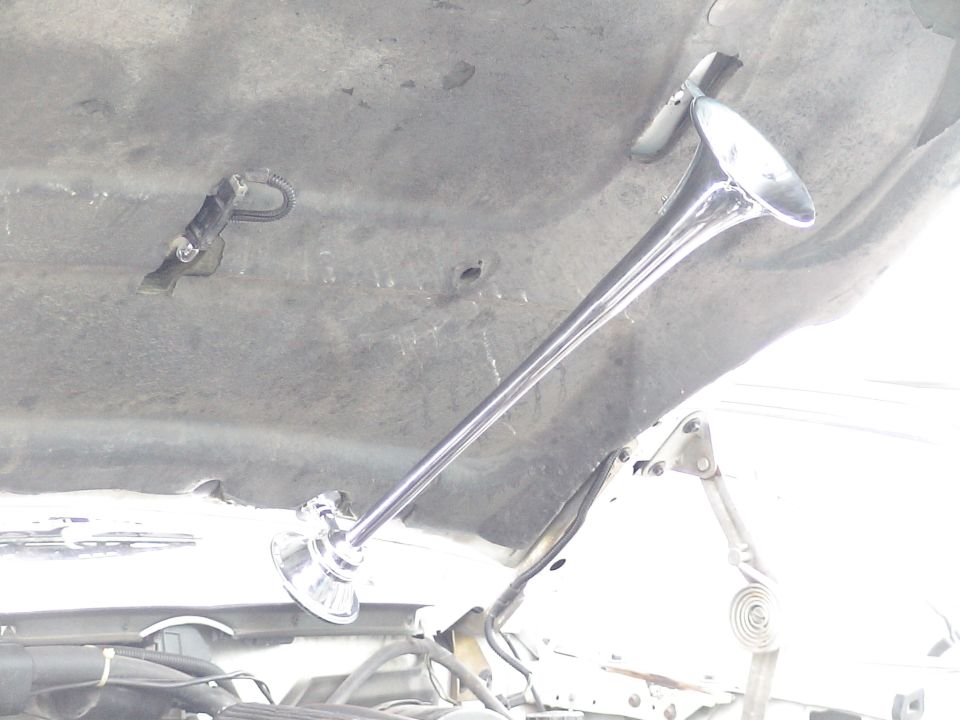 Chrome air horn mounted under the open hood of a vehicle.