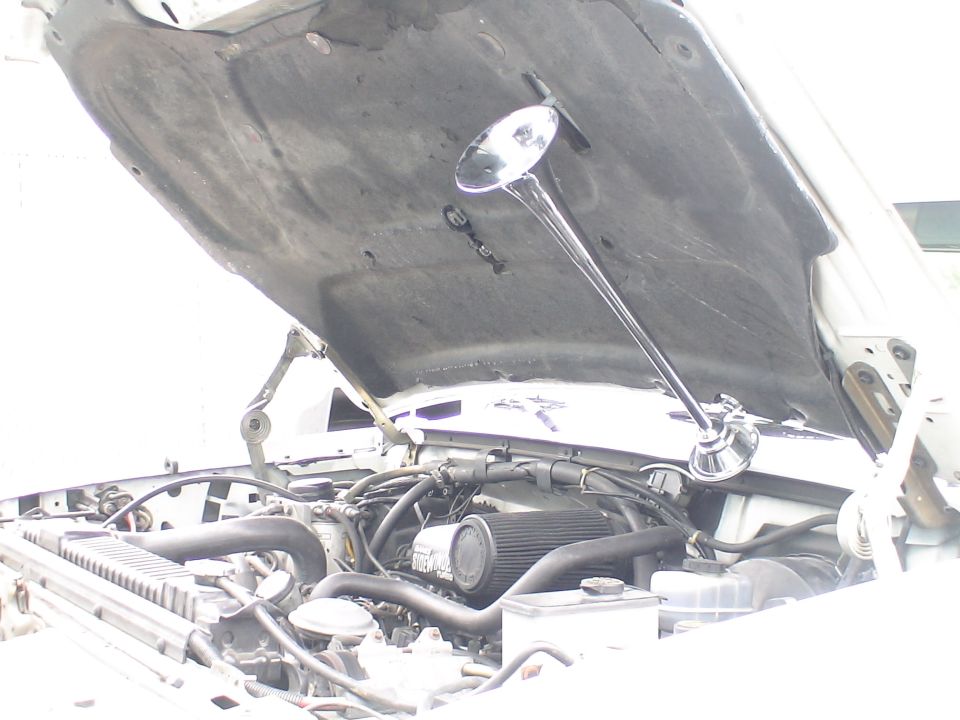 Vehicle hood open showing engine and a chrome mirror mounted to the hood.