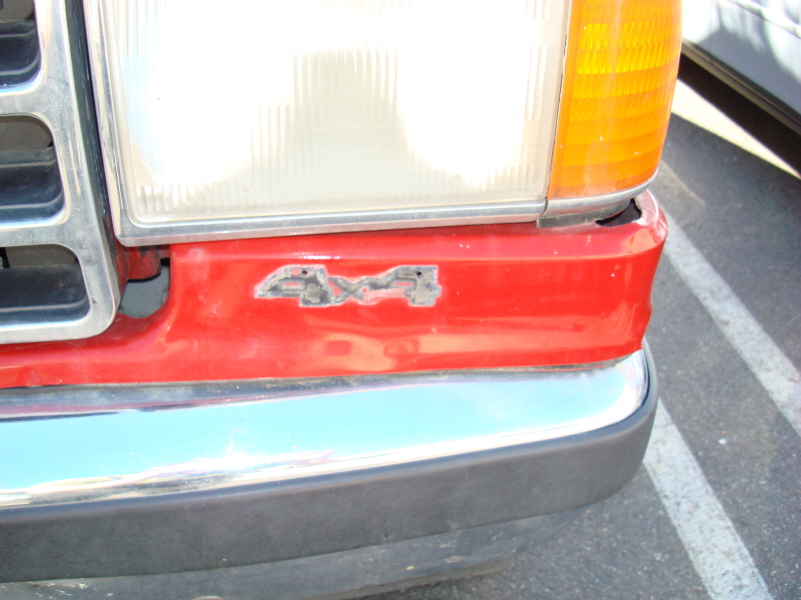 Close-up of red vehicle bumper with faded 4x4 emblem and chrome trim.