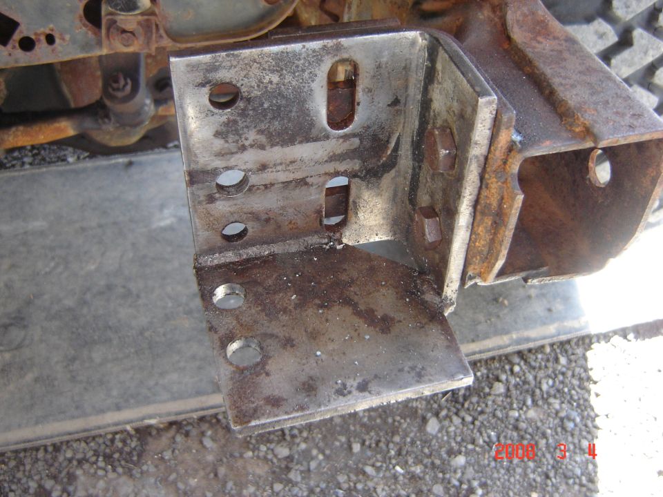 Rusty metal bracket with bolt holes attached to vehicle frame.