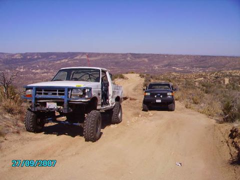 1990 Ford Bronco - A lifted white Ford pickup truck with a blue front brush guard is parked on a dirt road in a desert landscape. A black Ford pickup truck is…