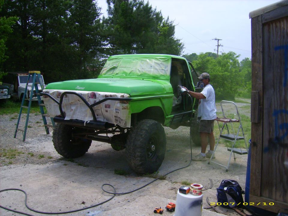 Lifted Bronco being spray-painted lime green with masked-off grille and windshield