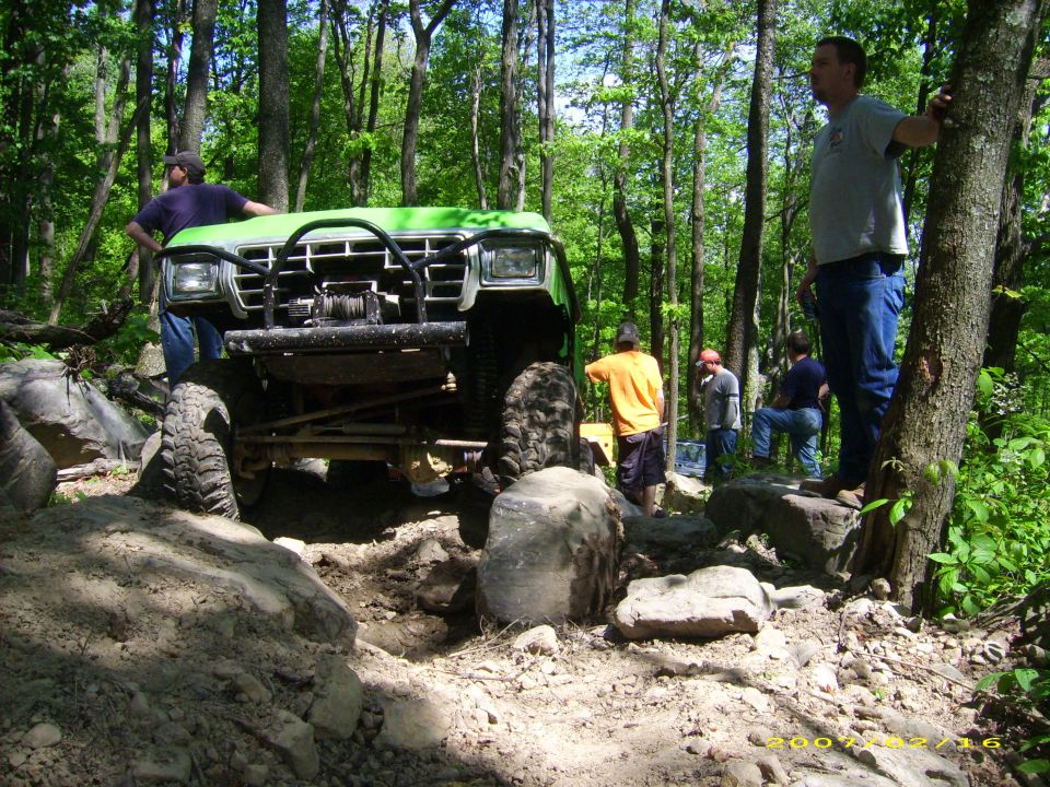 Green off-road vehicle on a rocky trail with people watching.
