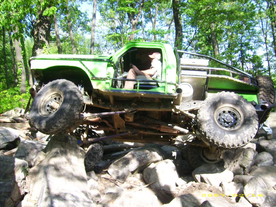 Green off-road truck with large tires climbing over rocks on a trail.