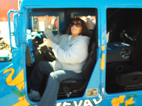 1978 Ford Bronco - A woman wearing sunglasses and a grey hoodie is sitting in the driver's seat of a bright blue vehicle, holding onto the steering wheel. The…