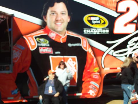 1978 Ford Bronco - A large mural of a NASCAR driver in racing attire is displayed on the side of a vehicle. Two people are standing in front of the mural.