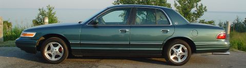 1996 Mercury Grand Marquis - Side profile of a 1996 Mercury Grand Marquis sedan parked outdoors near water.