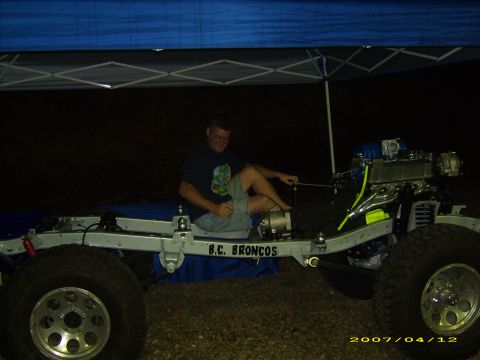 1978 Ford Bronco - A man works on a Ford Bronco chassis, which has the engine and suspension components attached.