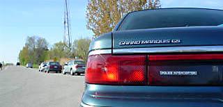 1996 Mercury Grand Marquis - A teal 1996 Mercury Grand Marquis GS with a 'POLICE INTERCEPTOR' badge is parked on a road with other vehicles.