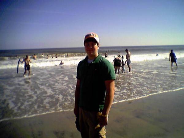 guy in a green shirt and hat on a beach with people in the ocean